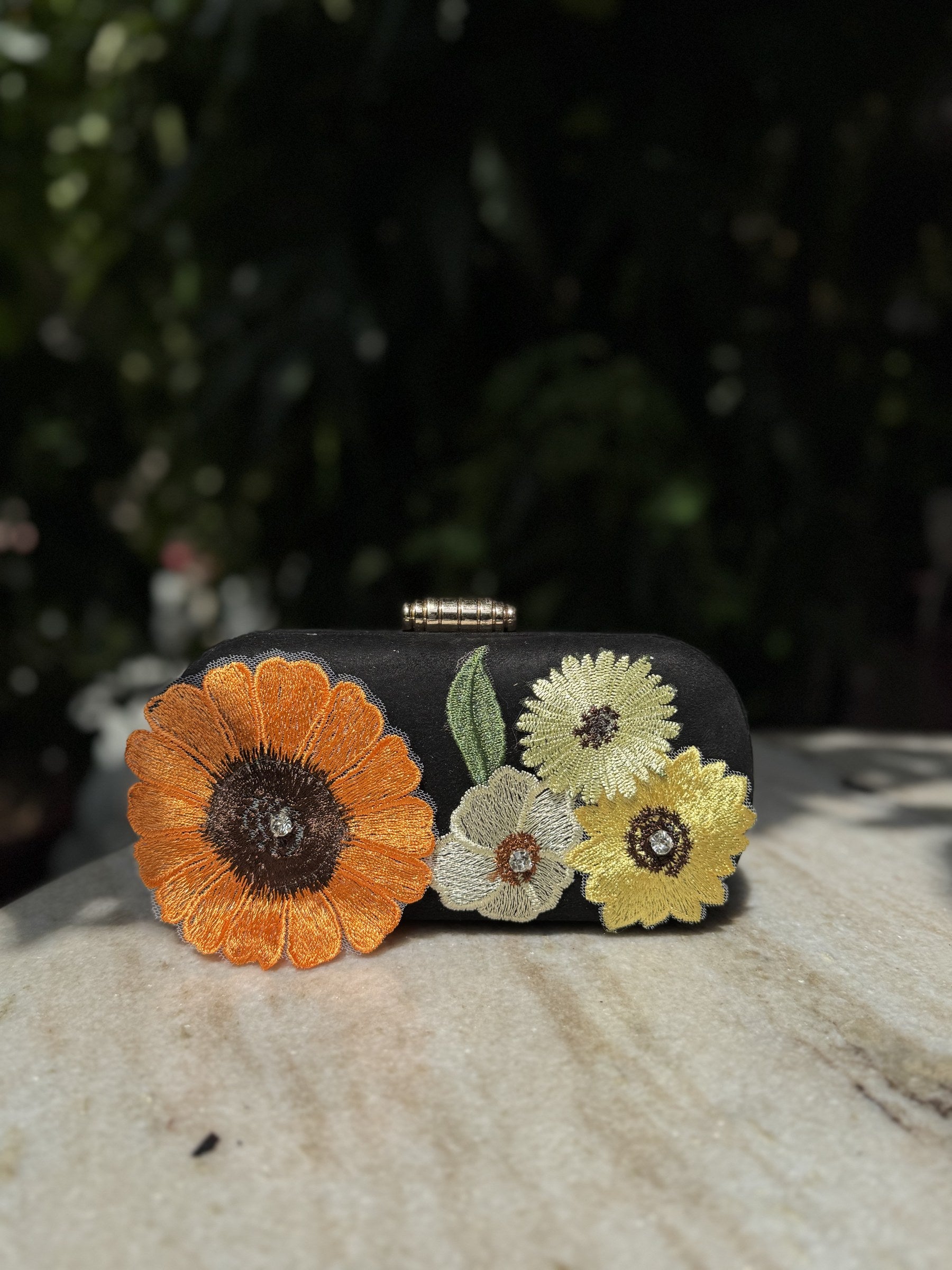 Bloom Box floral embroidered clutch displaying its multicolored flower stitching and gold-tone sling chain.
