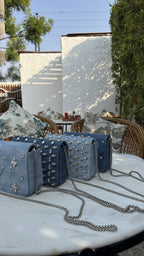 Top angle view of the Frosted Denim sling, showing the zip opening and metal hardware attachments.