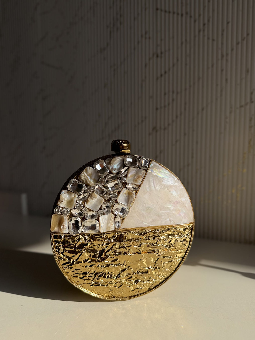 The Gilded Muse oval clutch held, displaying its sleek, light-reflecting gold surface.