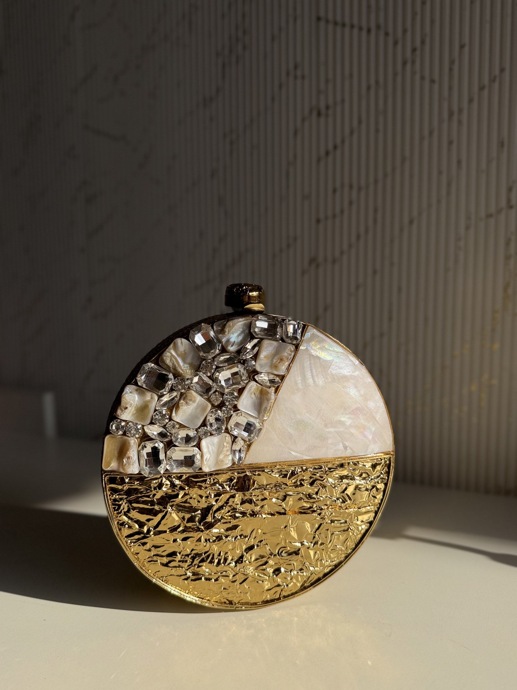 The Gilded Muse oval clutch held, displaying its sleek, light-reflecting gold surface.