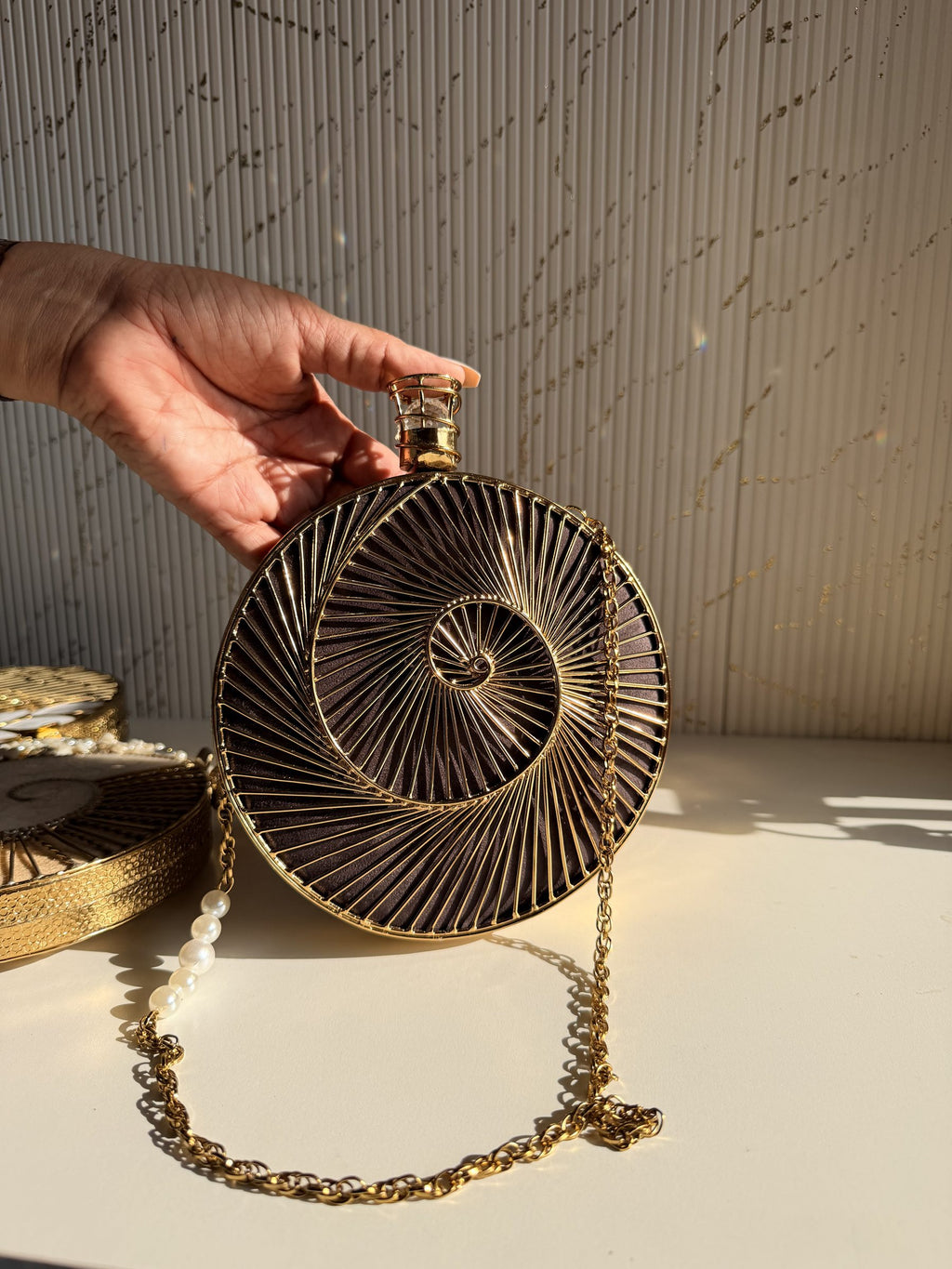 Lifestyle shot of the Gilded Muse brass clutch next to gold jewelry and raw silk coordinates.