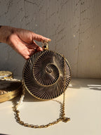 Lifestyle shot of the Gilded Muse brass clutch next to gold jewelry and raw silk coordinates.