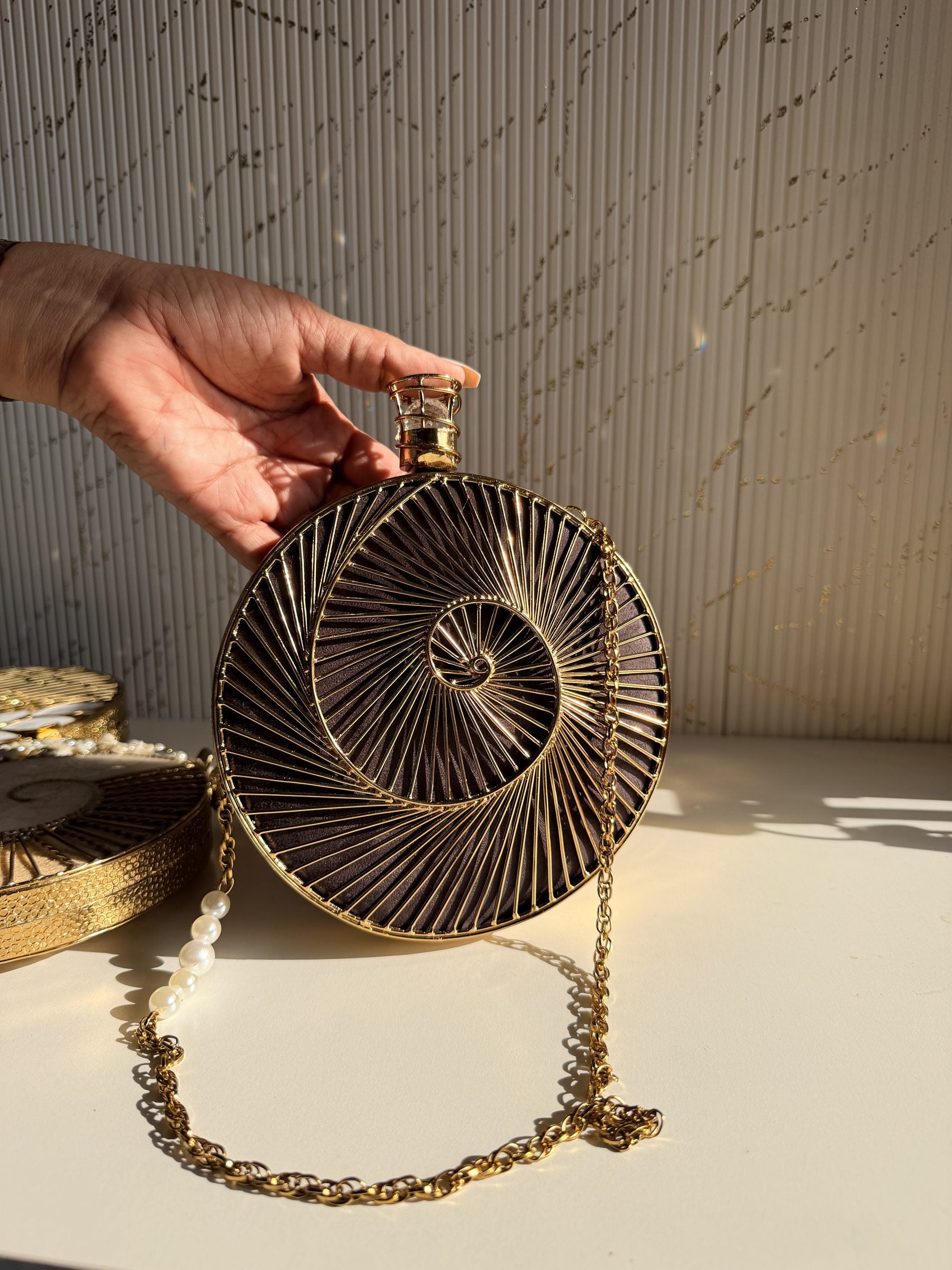 Lifestyle shot of the Gilded Muse brass clutch next to gold jewelry and raw silk coordinates.