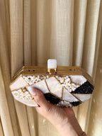 The Gilded Muse oval clutch displayed on a marble surface with sangeet coordinates.