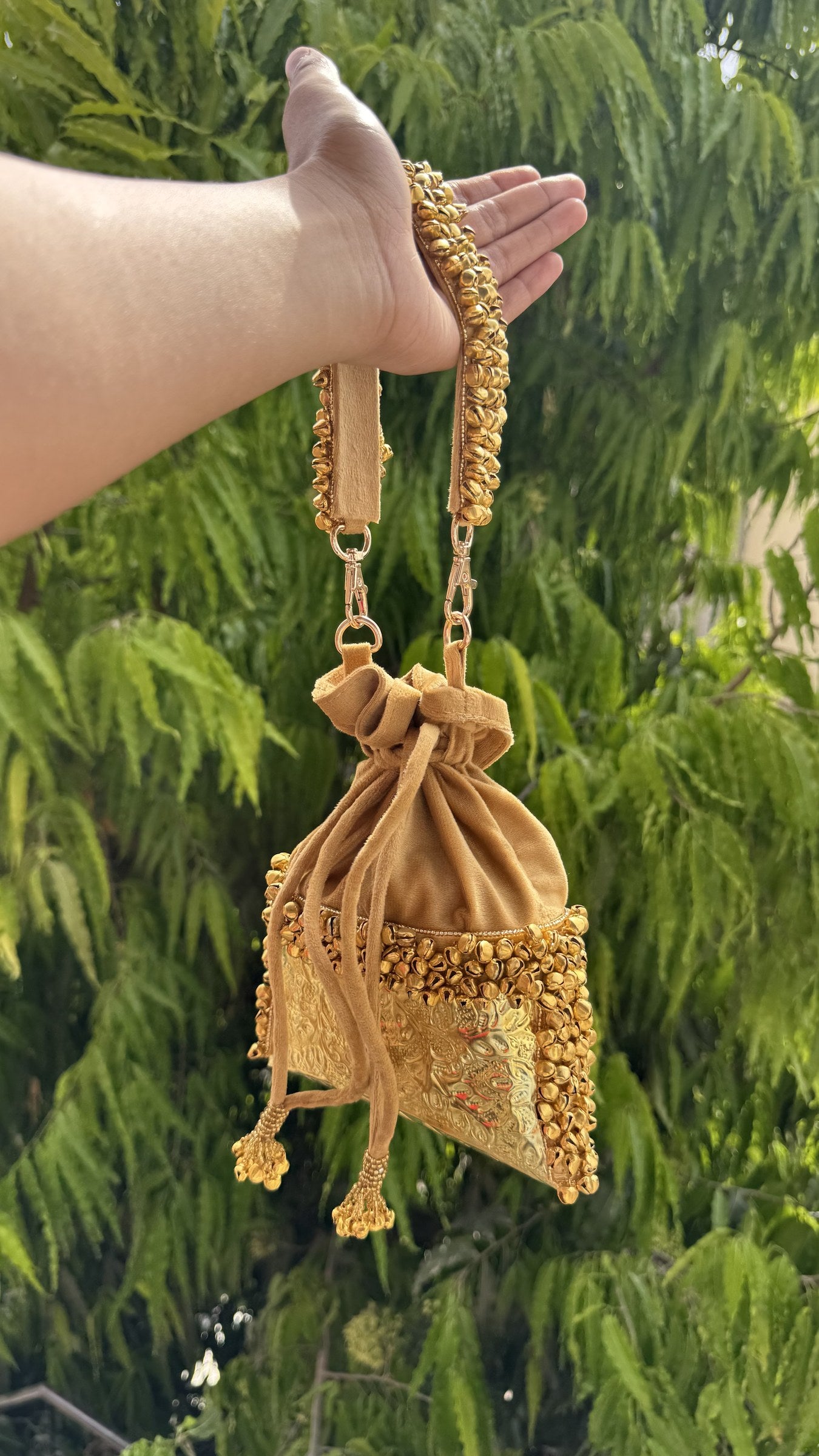 Handheld view of the Jhankar Potli demonstrating its wristlet drape and size proportion.