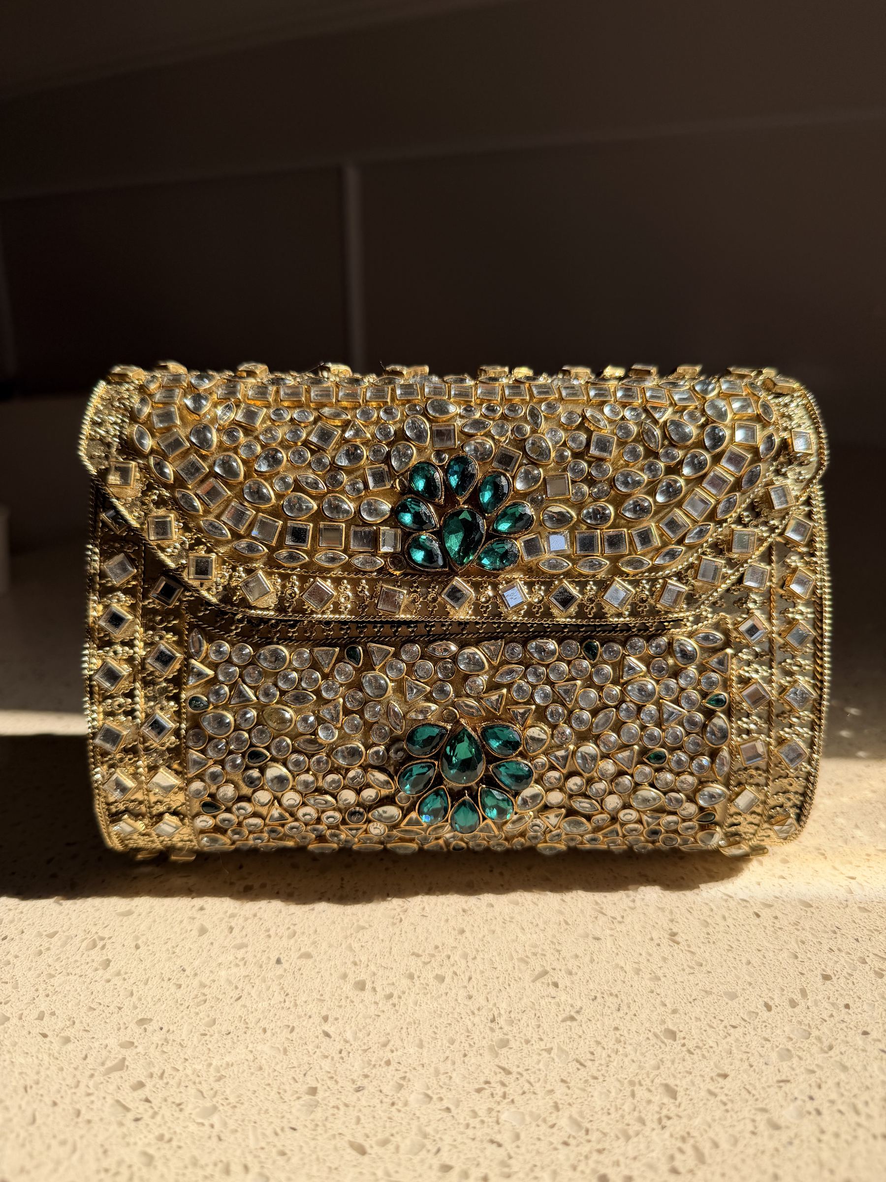 Kundan Peacock Heritage Clutch displaying its gold Kundan stones, green velvet, and brass peacock clasp.