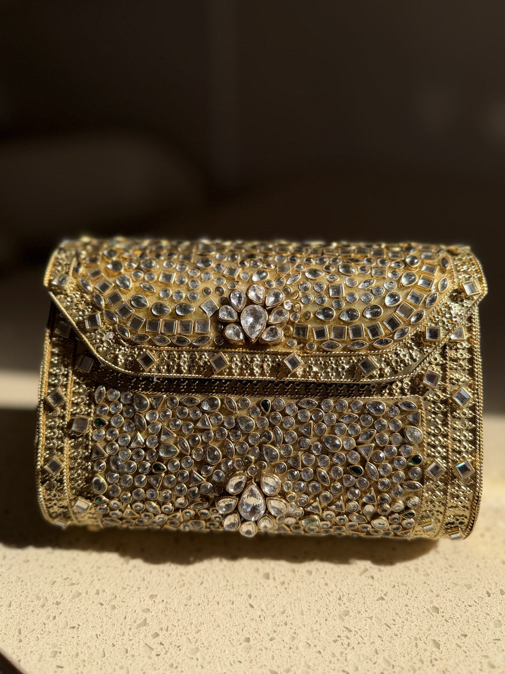 Side view of the structured Kundan clutch showing its gold metal border and velvet lining.