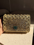 The Kundan Peacock clutch held by its beaded wristlet handle, showing handheld carry style.