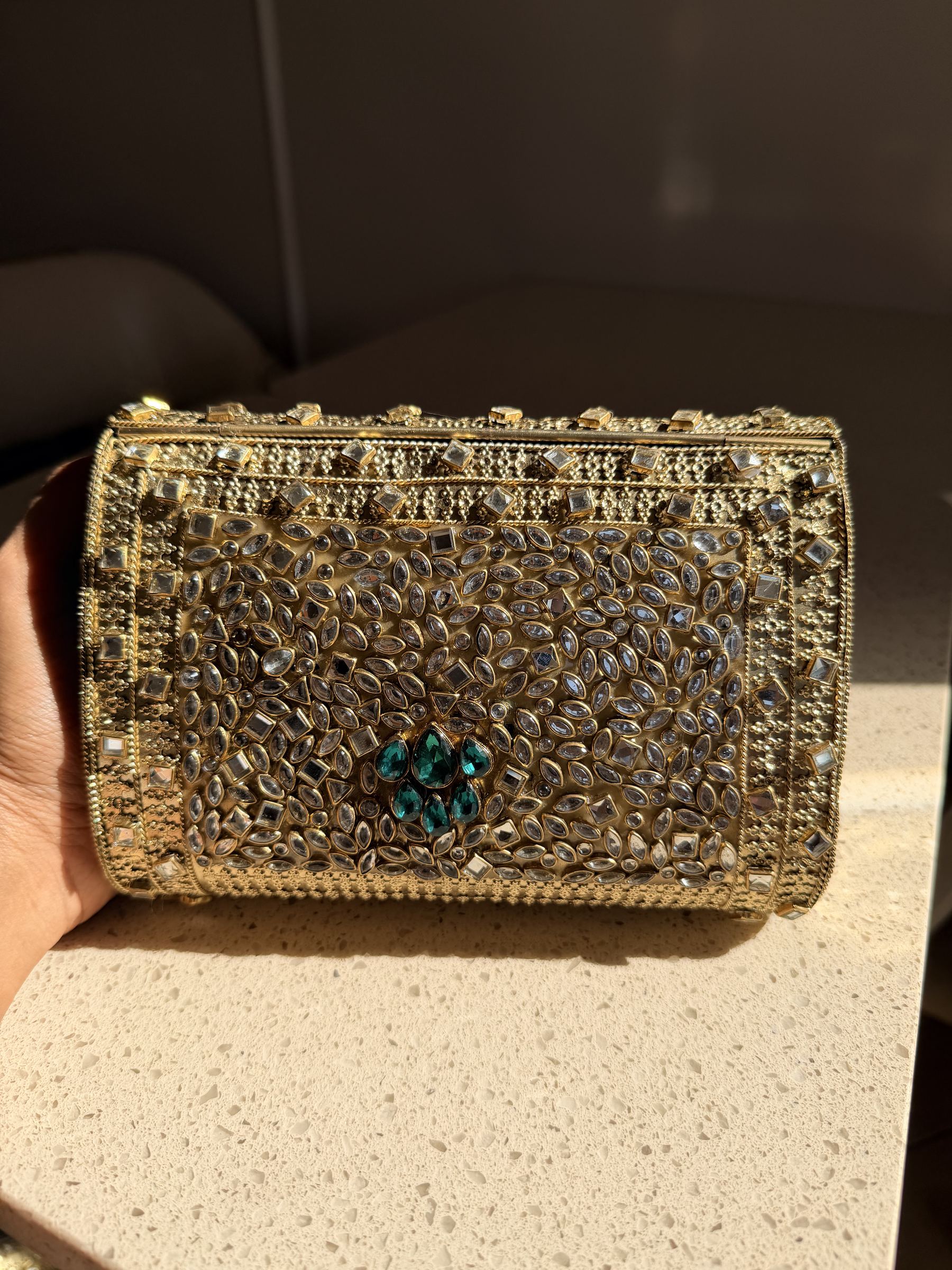 The Kundan Peacock clutch held by its beaded wristlet handle, showing handheld carry style.