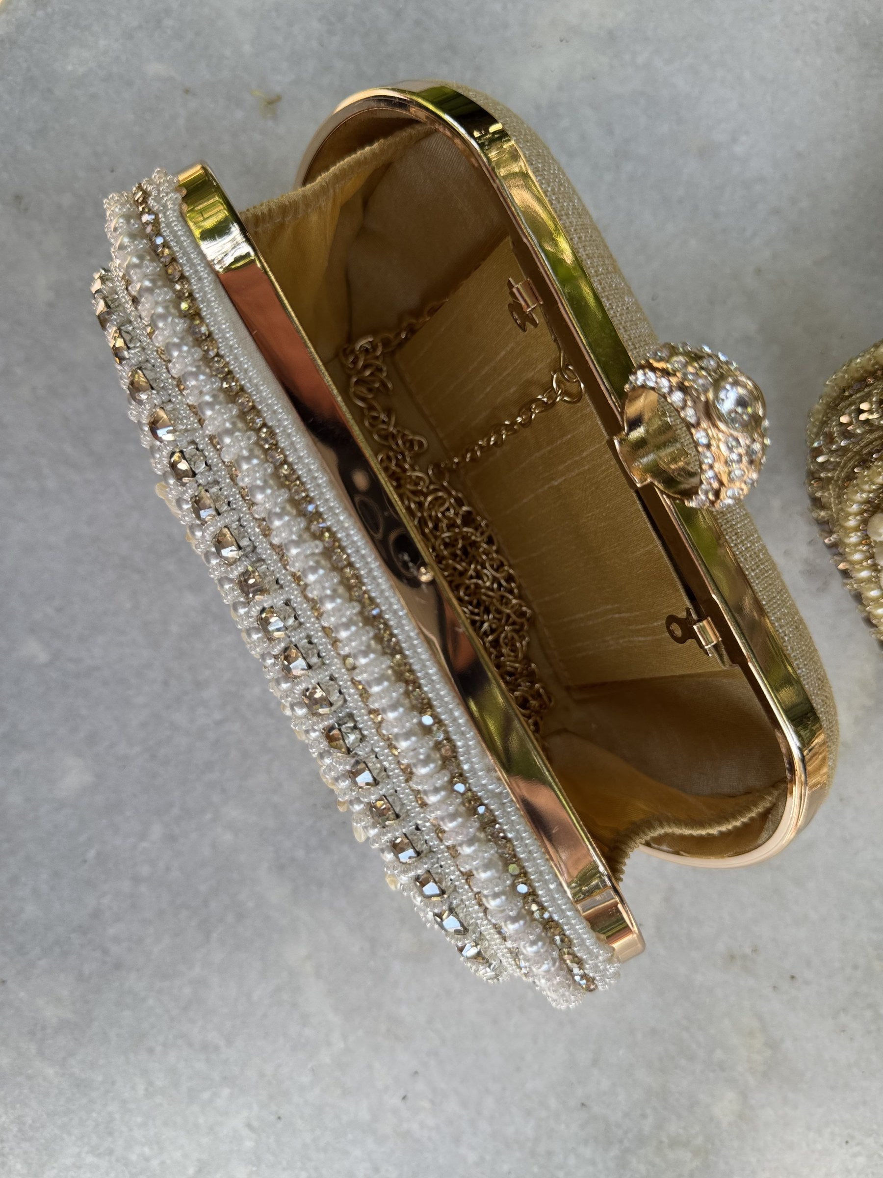 Flat lay of the Luxe Grip clutch next to matching gold sandals and pearl jewelry.