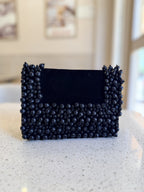 Front view of the Noir Pearl Edit Clutch showing its black fabric base and white pearl detailing.