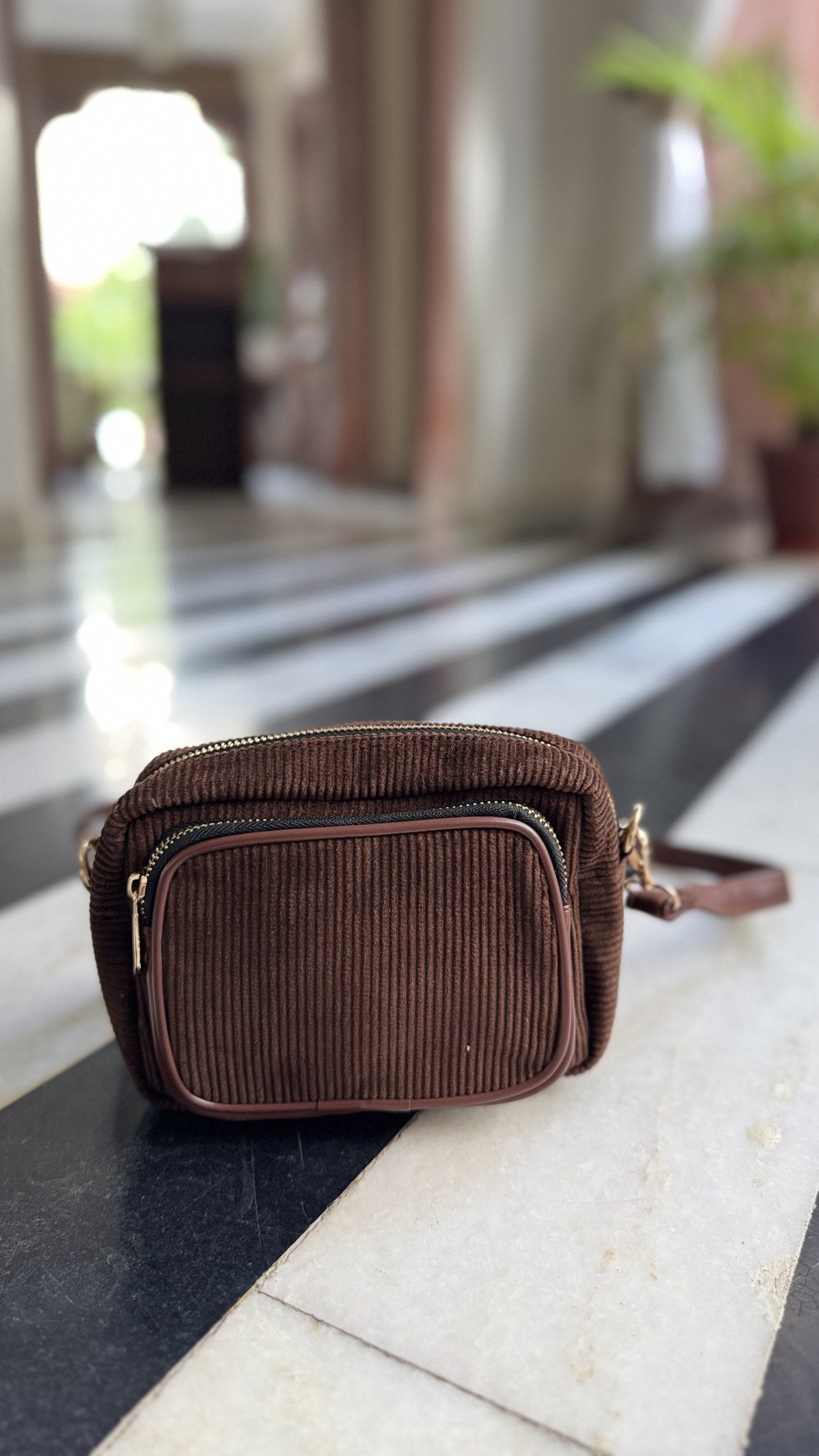 The Corduroy Edit sling displayed alongside cozy autumn leaves and a knit scarf.