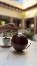 The Orb round wooden clutch displaying its spherical shape, circular wood grain, and gold brass borders.