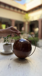 The Orb round wooden clutch displaying its spherical shape, circular wood grain, and gold brass borders.